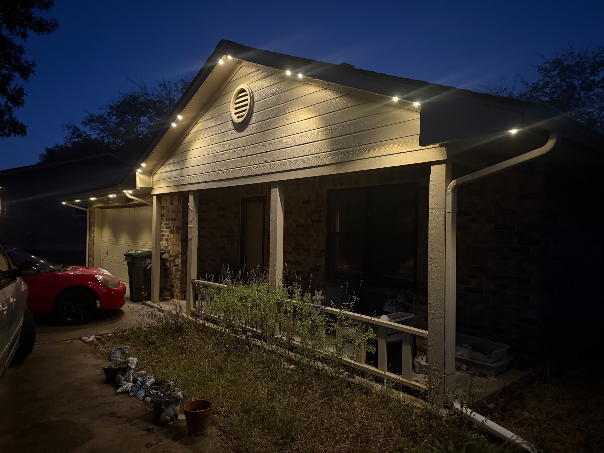 Brick home with a covered porch and warm-white permanent lights mounted behind the fascia at dusk