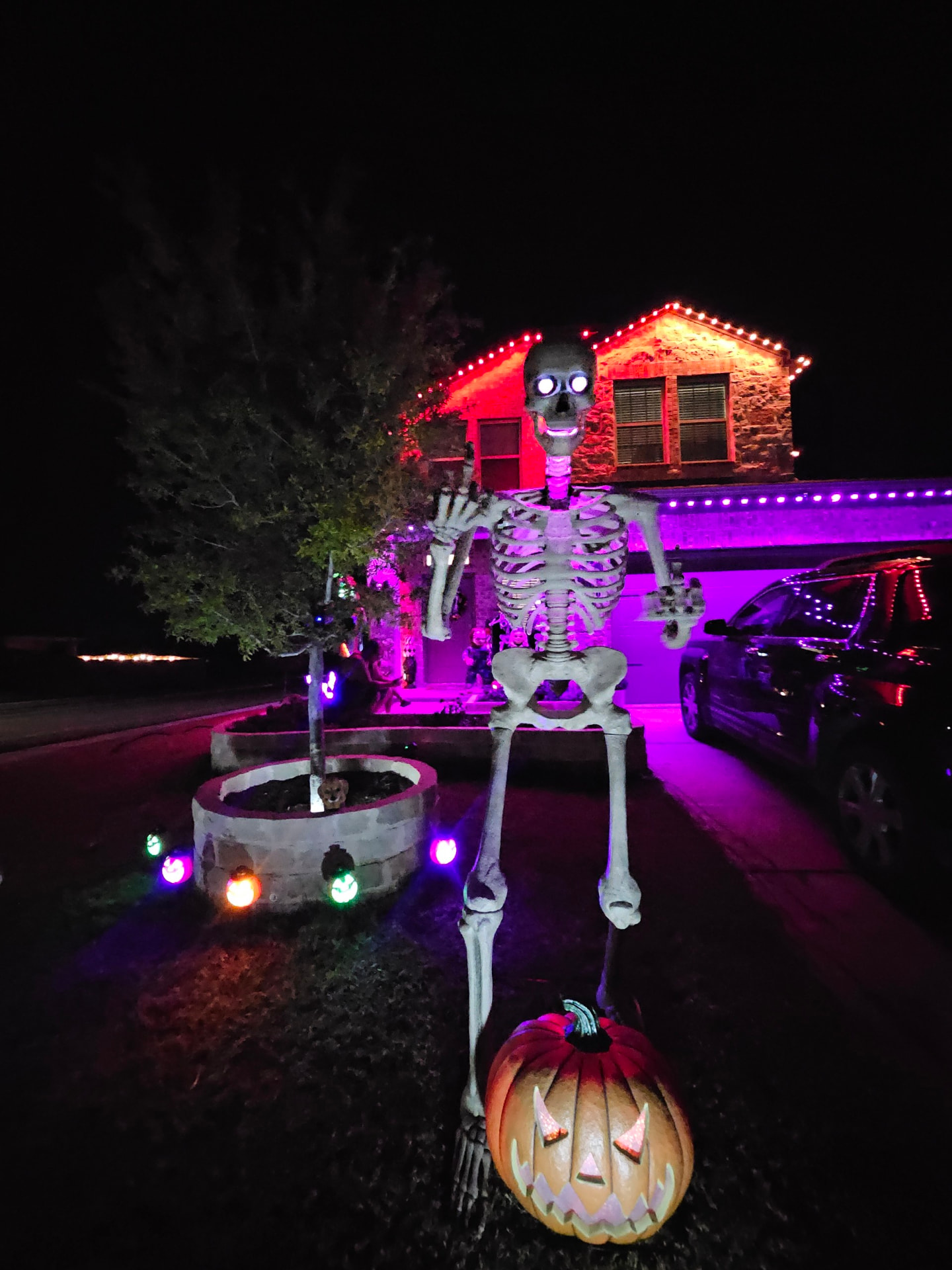 Giant skeleton and pumpkin in front of a home with red and purple permanent roofline lighting