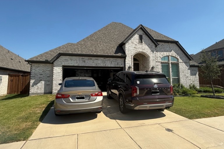 Light-brick home with arched entry and two vehicles in the driveway during the day, lights off
