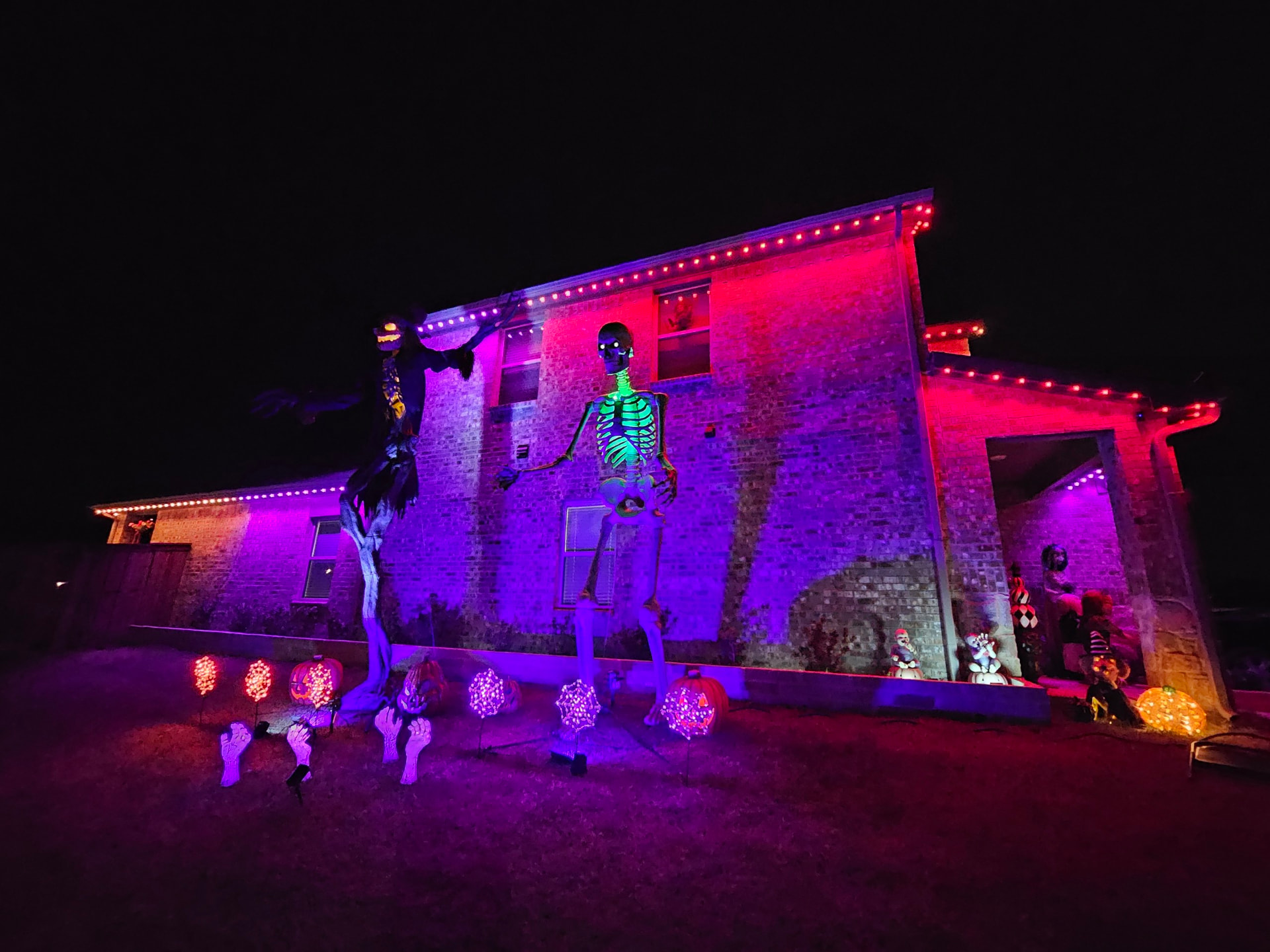 Two-story brick home with red and purple permanent roofline lighting and Halloween skeleton decorations