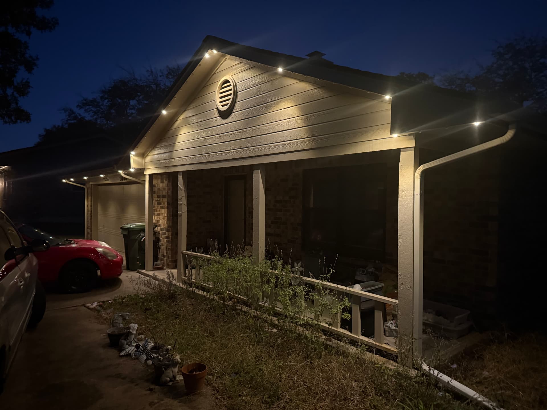 Warm-white permanent LED nodes mounted beneath the fascia of a covered porch and garage roofline